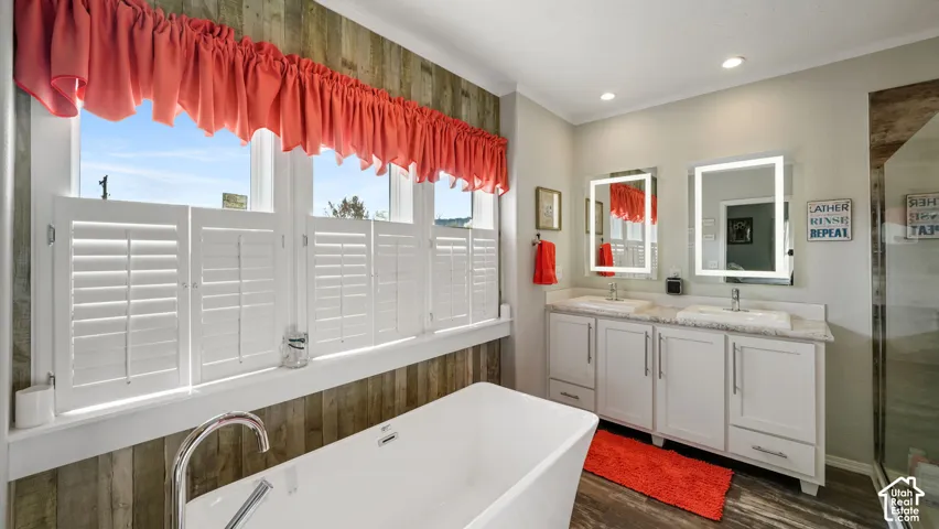 Freestanding soaking tub, dual-sink vanity with light-stone countertop, illuminated wall mirrors, wood-finish wall paneling, and interior plantation shutters