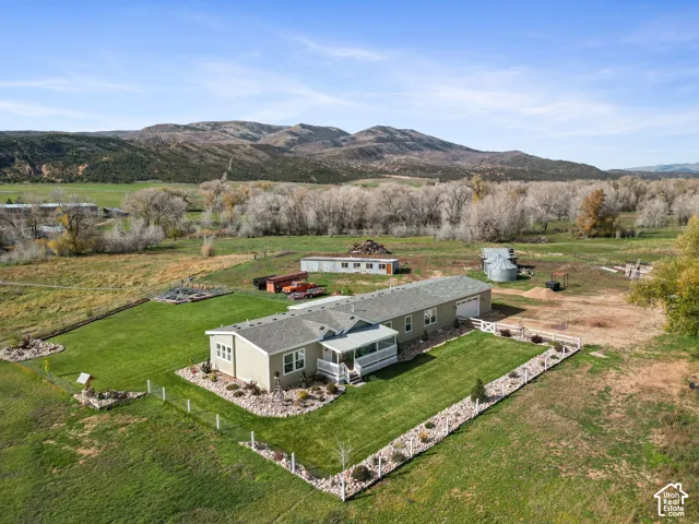 Single-level exterior with a covered porch, attached garage, fenced perimeter, stone landscape edging, and mountain backdrop