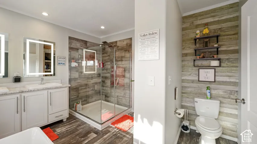Bathroom featuring a dual-sink vanity with light-toned cabinetry and solid surface countertop, backlit vanity mirrors, and a glass-enclosed shower with wood-finish tile surround