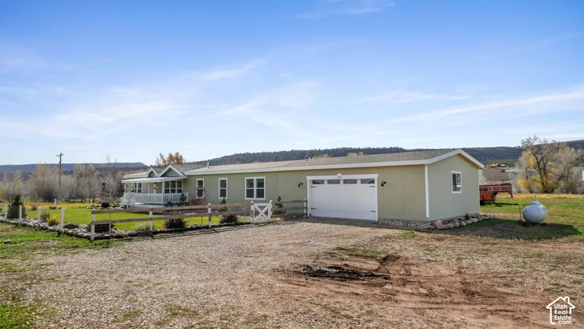 Single-level residence with pale green siding, attached two-car garage, covered front porch, and perimeter post-and-rail fencing