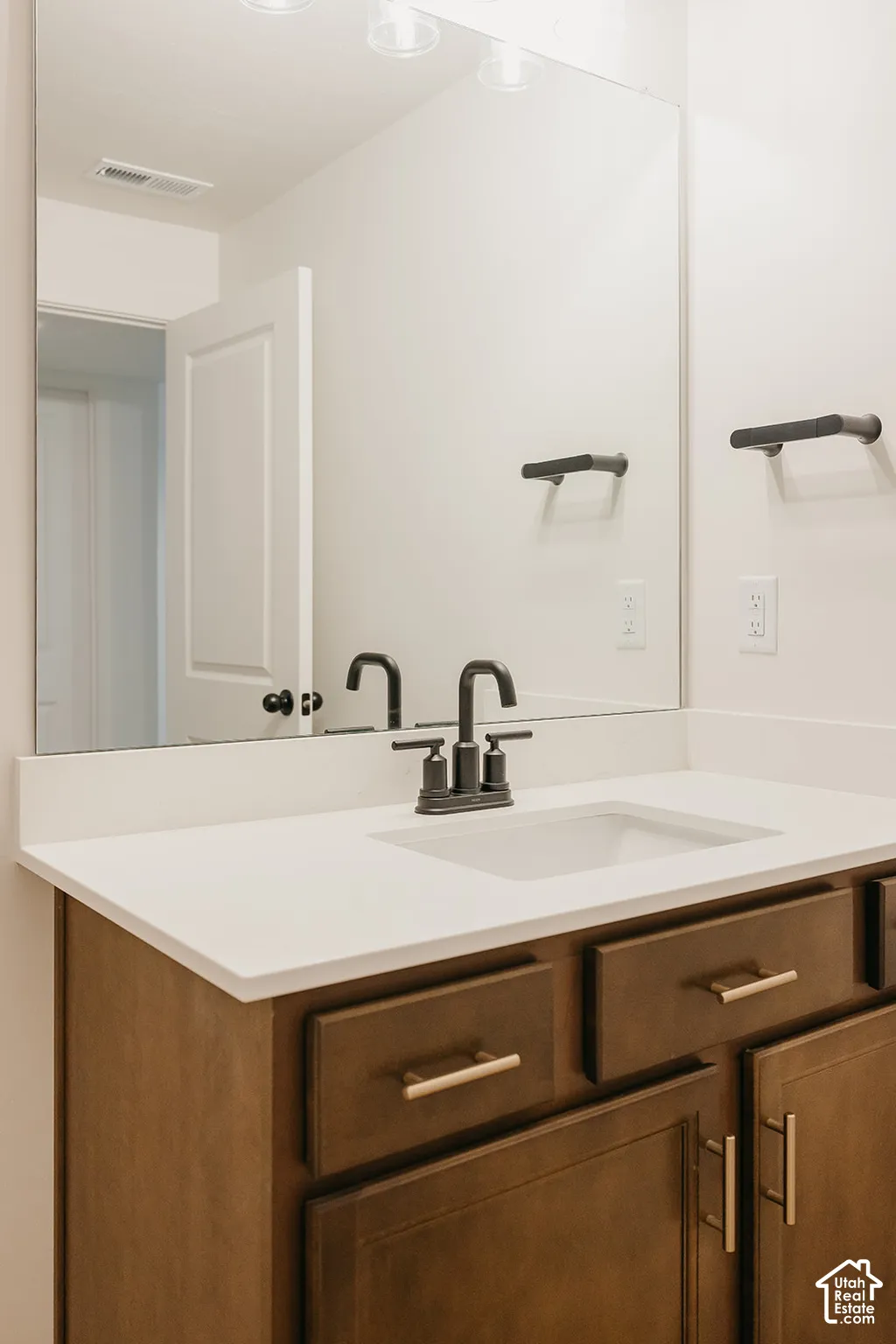 Bathroom vanity featuring a solid-surface countertop with an integrated rectangular basin, dark wood-finish cabinetry, matte black widespread faucet, and a large wall-mounted vanity mirror