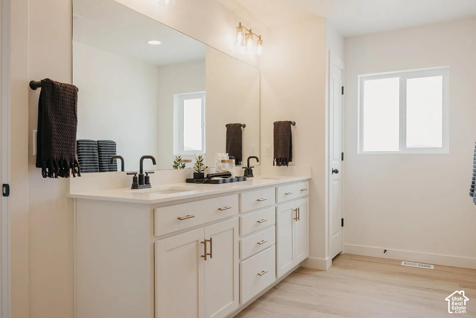 Dual-sink vanity featuring white shaker-style cabinetry, quartz countertop, matte black fixtures, and a wall-to-wall mirror with mounted lighting