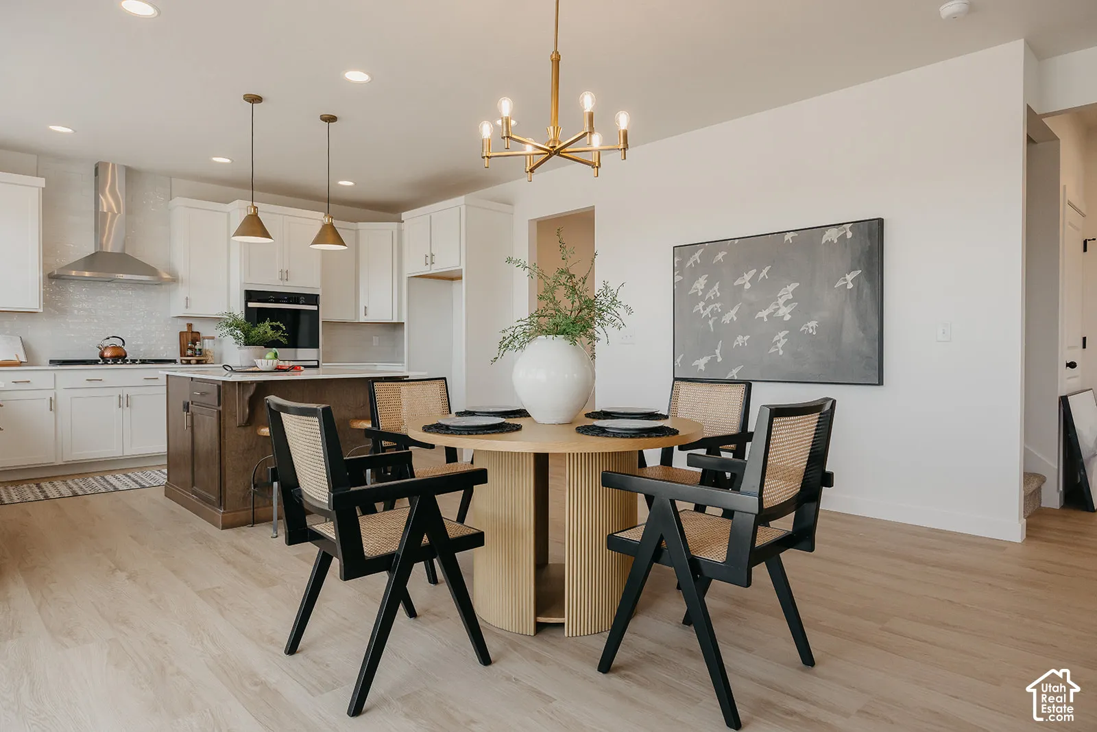Kitchen featuring white cabinetry, wood-finish flooring, a stainless steel range hood, an island with a decorative base, and a brass-tone chandelier