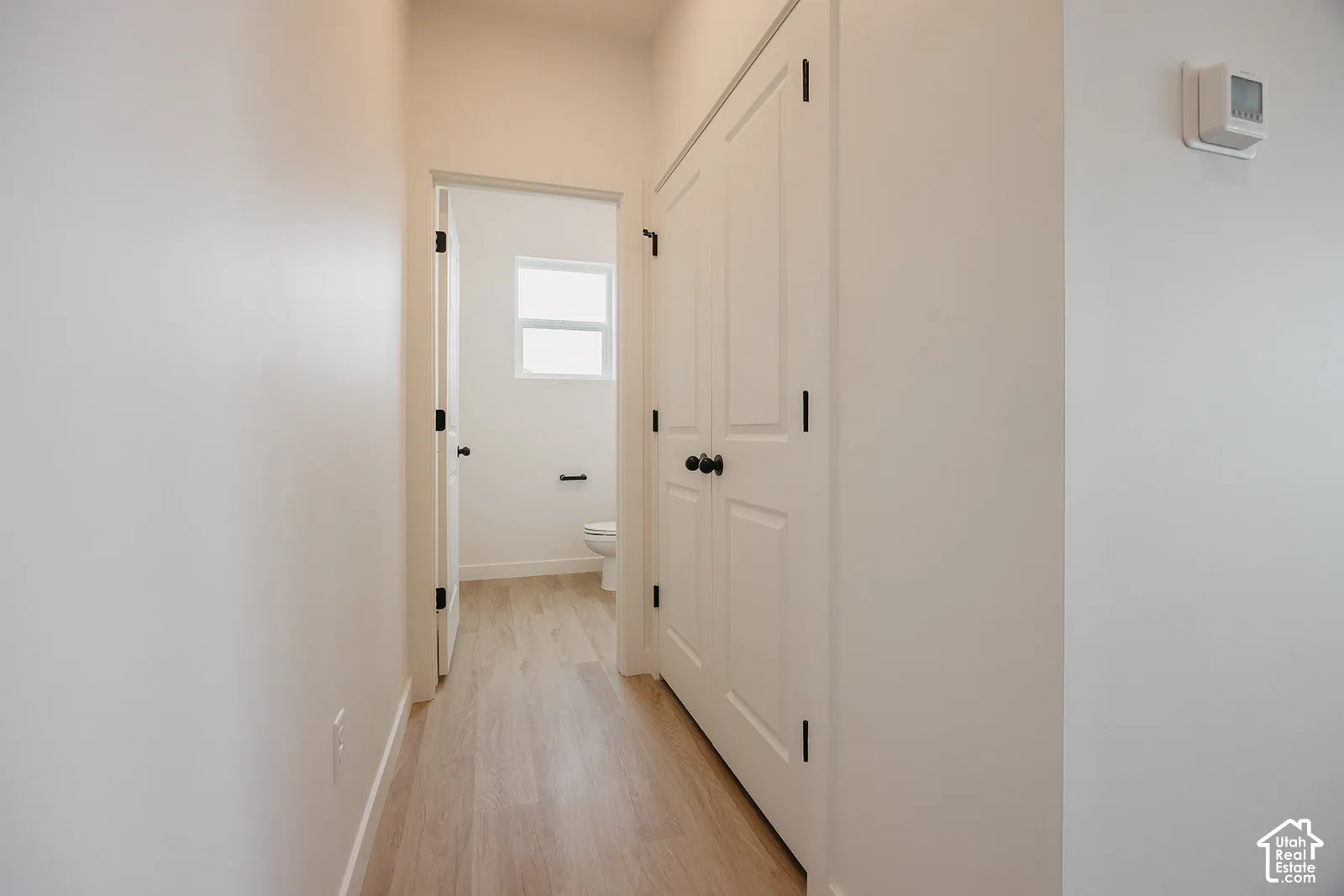 Hallway featuring wood-finish flooring, double-panel closet doors with matte black hardware, and an interior passage door with matching hardware