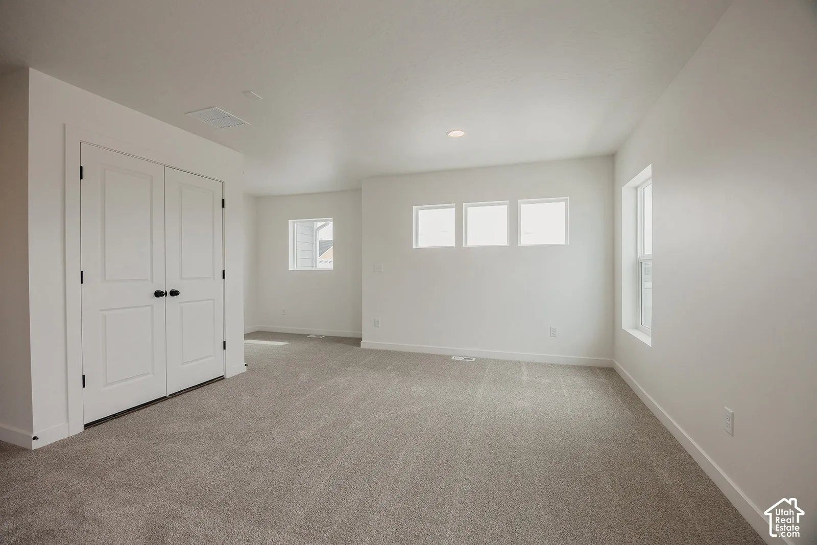 Neutral-toned carpeted flooring, double-door closet with matte black hardware, and multiple windows providing natural light