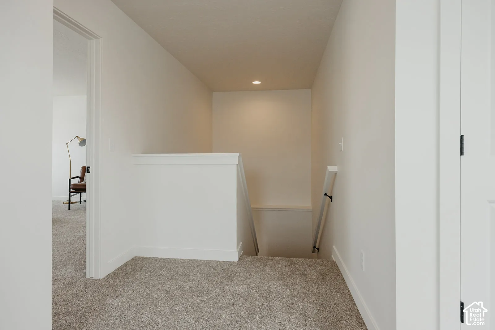 Neutral wall finishes, recessed ceiling lighting, carpeted flooring, and a half-wall staircase enclosure with a white-finish handrail