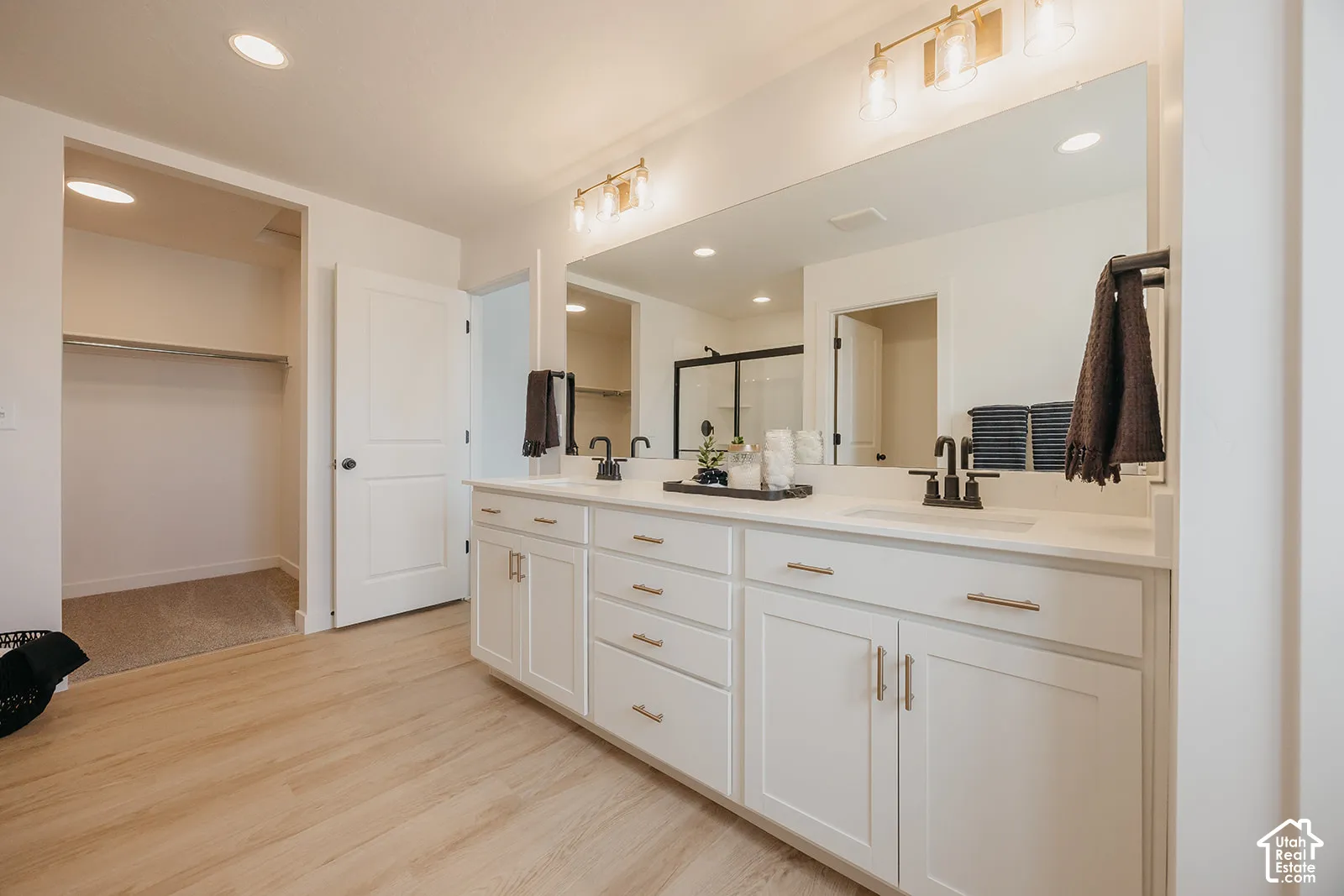 Double vanity featuring white cabinetry, light-toned stone-finish countertops, matte black plumbing fixtures, and a wide wall-mounted mirror