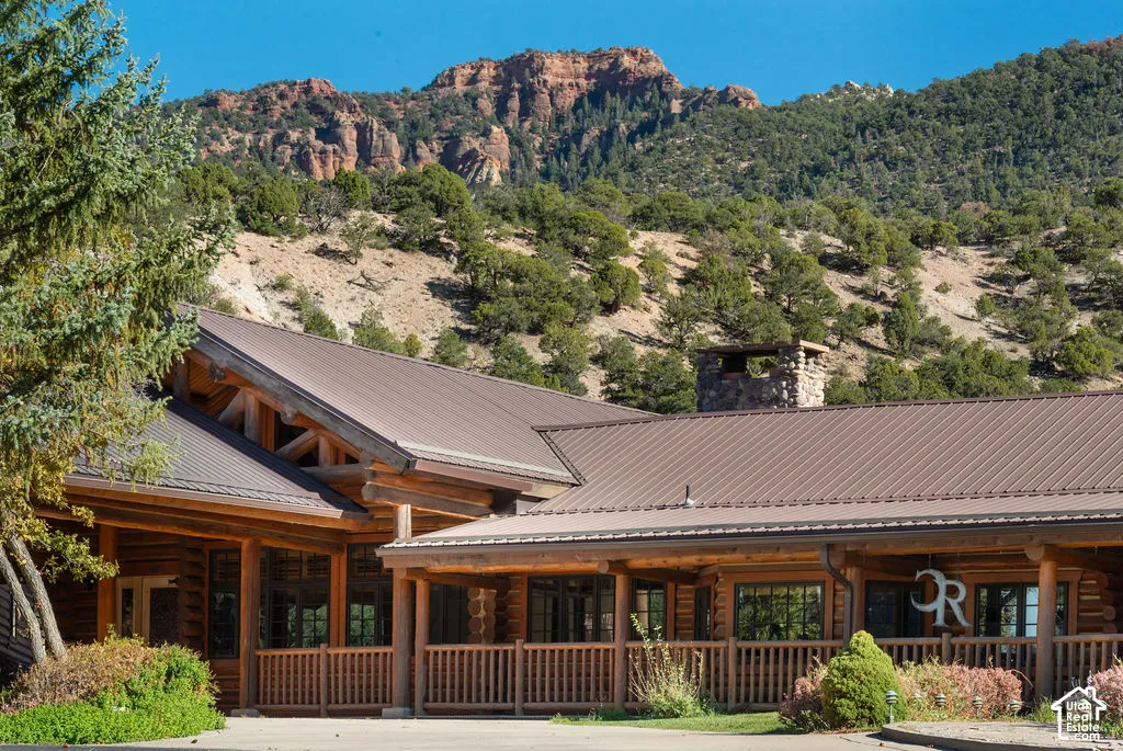 Log construction exterior featuring a metal roof, stone-clad chimney, and covered porch with wooden railings against a mountainous backdrop