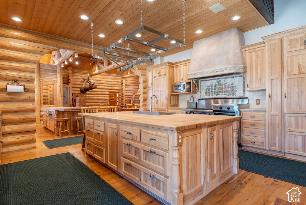 Kitchen featuring beautiful wood cabinetry, a large central island with a wood countertop, a stainless steel range with a custom range hood, recessed lighting, and log-style wall construction