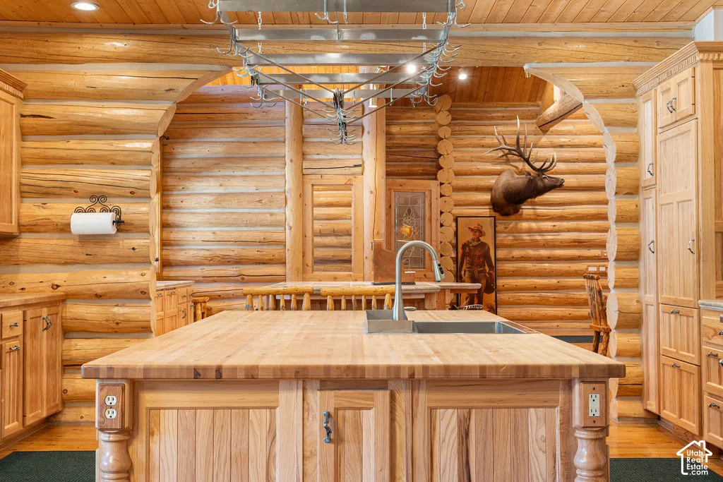 Kitchen featuring exposed log walls, a center island with a butcher block countertop and integrated sink, custom wood cabinetry, and a ceiling-mounted metal pot rack