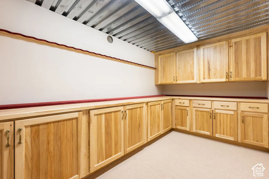 Walk-in safe with custom natural wood cabinetry with metal hardware, extensive built-in lower and upper storage, and industrial-style corrugated metal ceiling