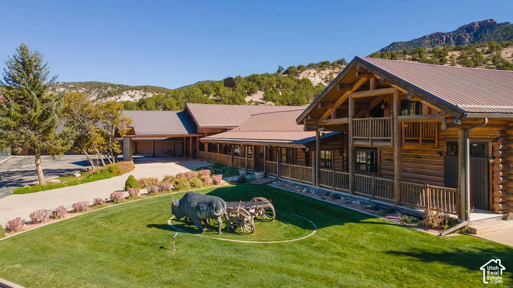 Log-constructed exterior featuring a metal roof, balconies, a sprawling lawn, and a mountainous backdrop