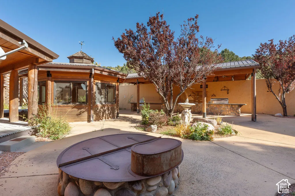 Outdoor living area featuring a stone-faced built-in kitchen, a covered patio structure, a custom hexagonal gazebo, a masonry-wrapped fire pit, and mature trees