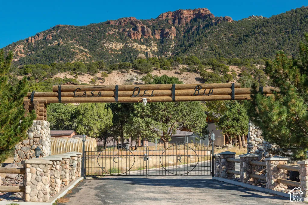 Gated entrance featuring stone pillar foundations, horizontal timber fencing, and a metal security gate, set against a mountainous backdrop with native vegetation