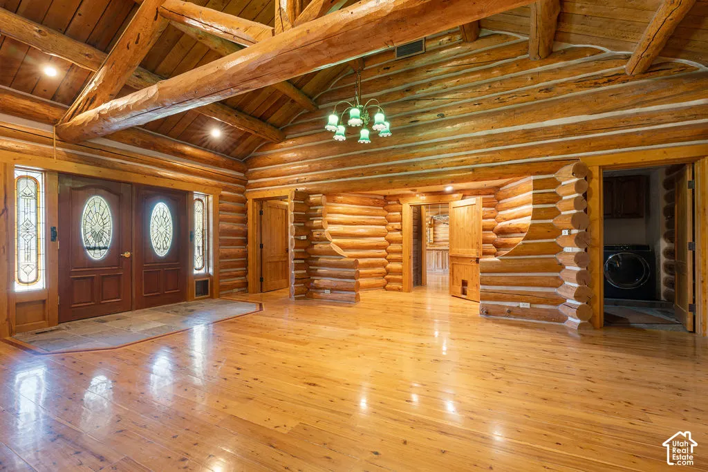 Expansive interior featuring exposed log walls, vaulted ceilings with heavy timber trusses, polished wood-finish flooring, and double entry doors.