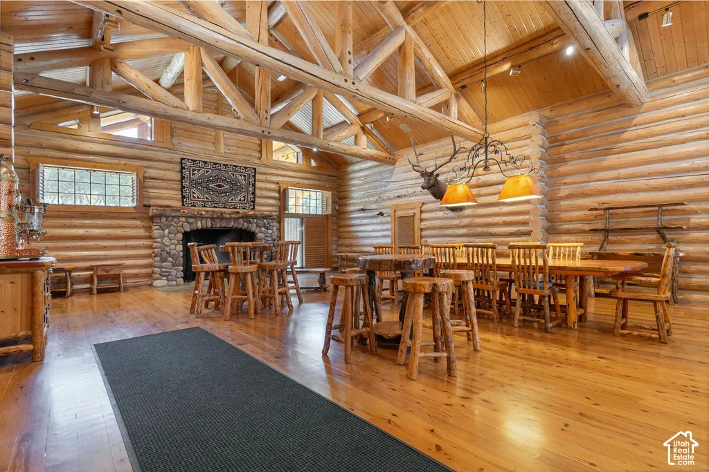 Great room featuring exposed timber truss ceiling, full log walls, hardwood flooring, and a natural stone fireplace surround