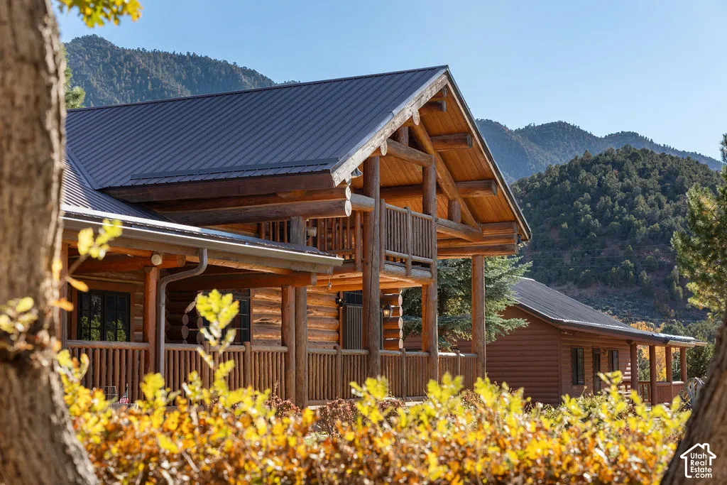 Log-construction exterior featuring a covered porch, upper-level balcony, metal roofing, and mountain backdrop