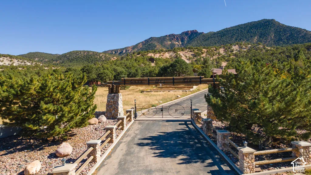 Gated entrance featuring stone pillar foundations, horizontal timber fencing, and a metal security gate, set against a mountainous backdrop with native vegetation