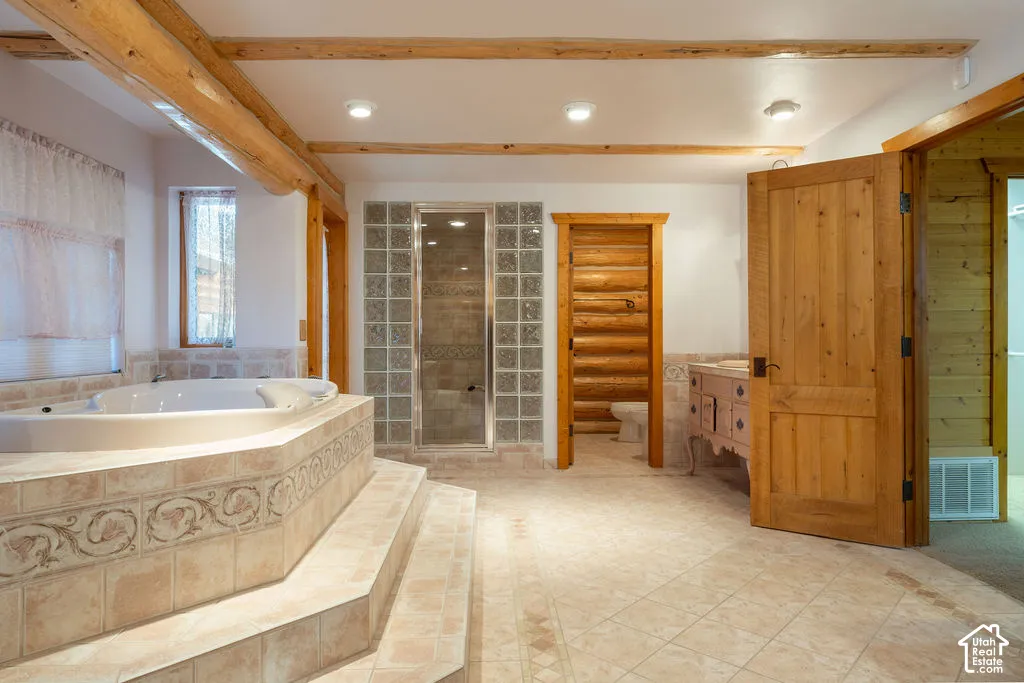 Primary bathroom featuring a raised platform with a jetted tub with tile surround, exposed log ceiling beams, and wood door and trim detailing