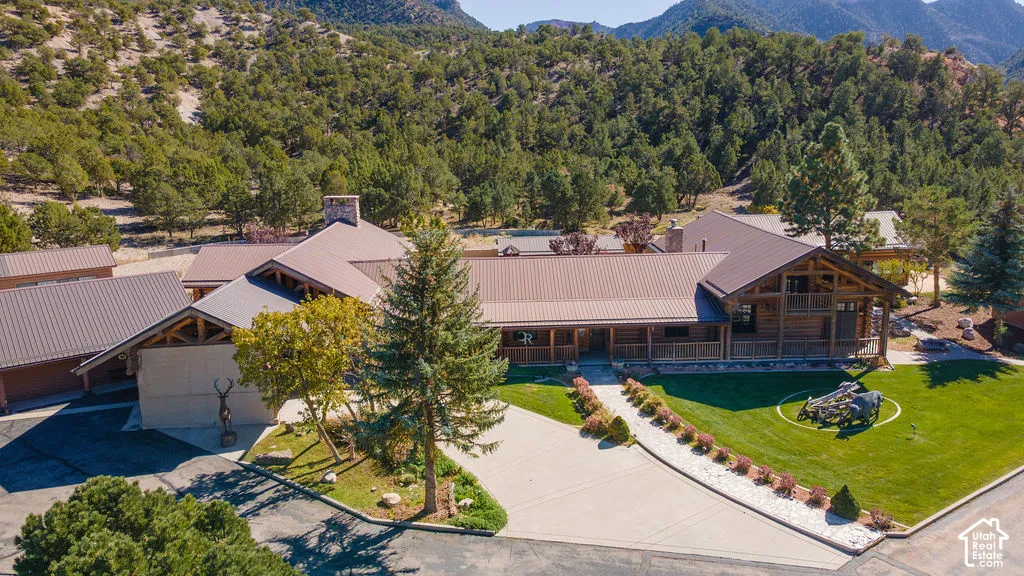 Expansive residence featuring a multi-gabled metal roof, timber-framed exterior accents, covered porch, stone chimney, and manicured lawn