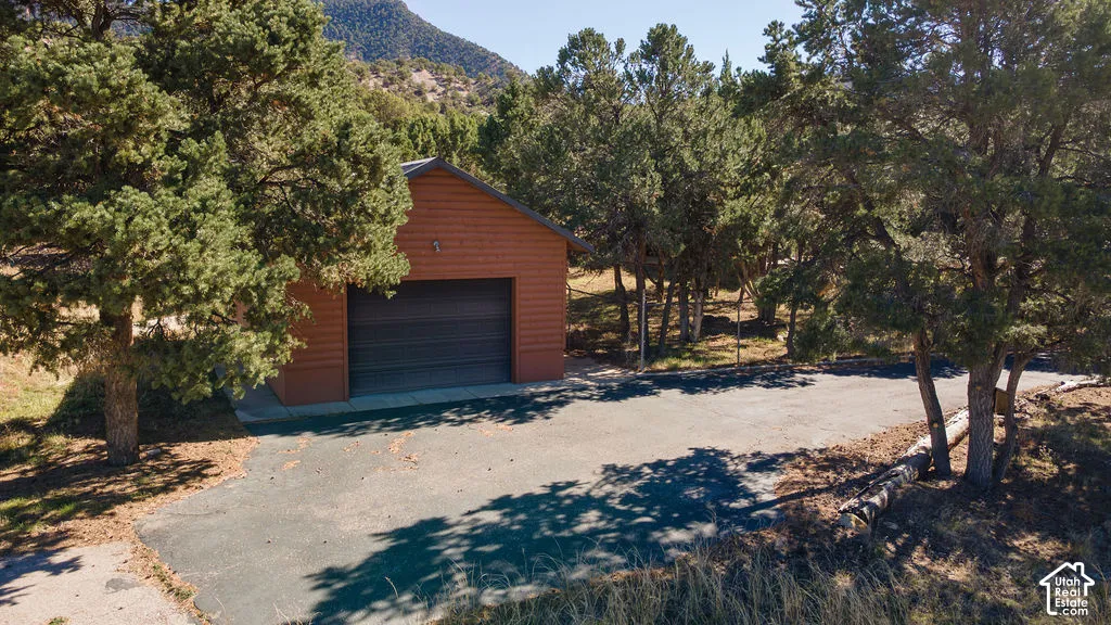 Detached garage with horizontal siding, an asphalt driveway, and mature trees against a mountainous backdrop