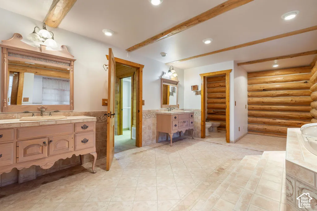 Primary bathroom with exposed timber ceiling beams, natural log wall accents, tile flooring, and dual custom vanities with integrated mirrors