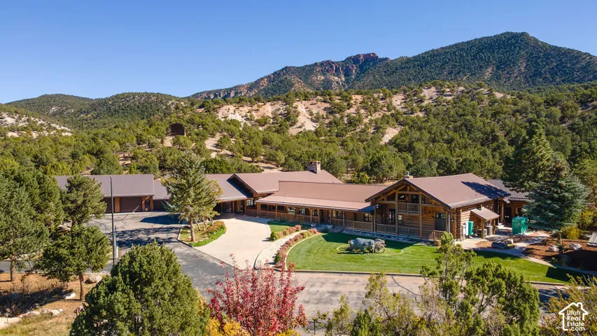 Log cabin exterior featuring a multi-gabled metal roof, expansive covered porch, integrated multi-car garage, and manicured landscaping set against a mountain backdrop.