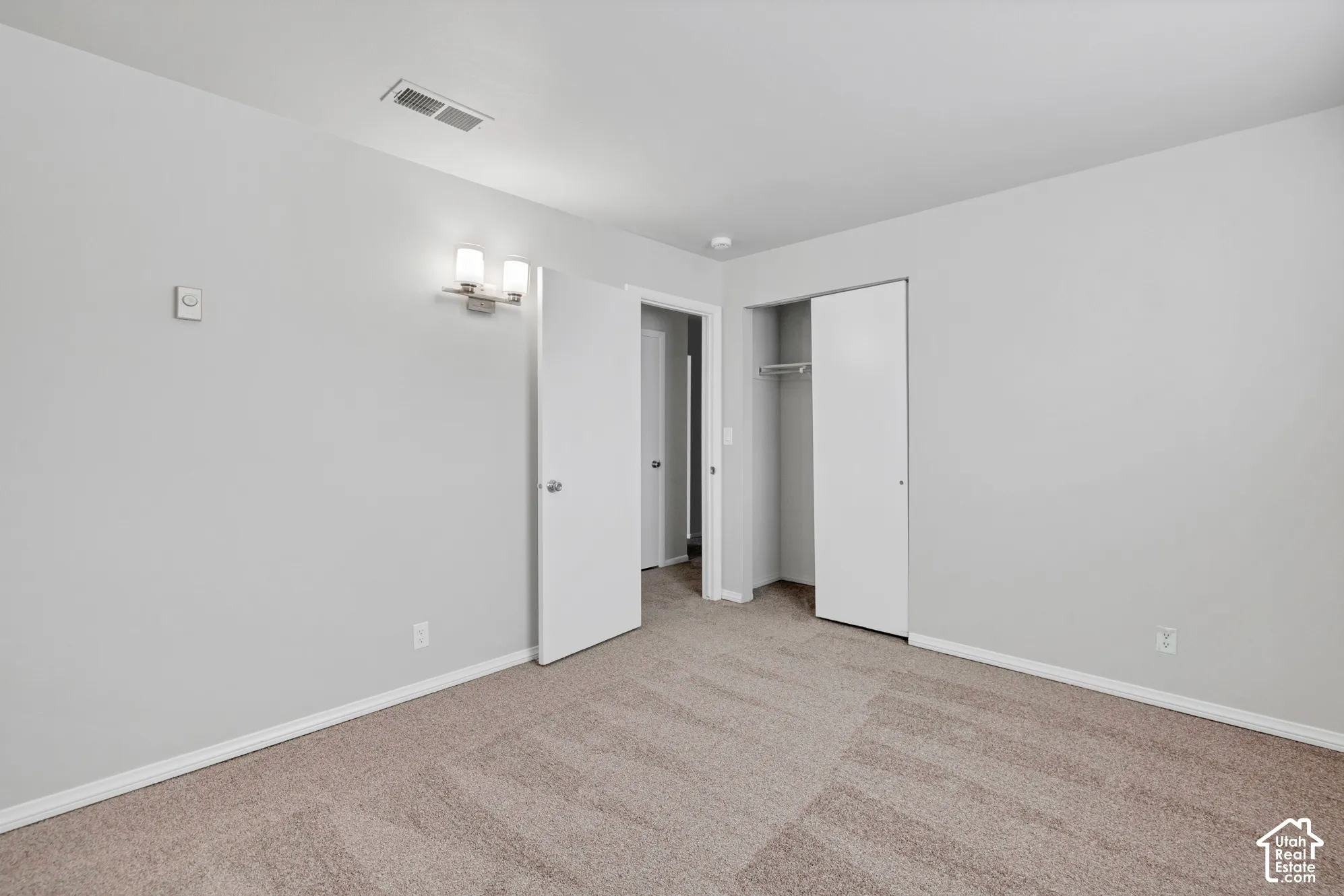 Neutral-toned carpeting, dual-light wall sconce, and built-in closet with integrated shelving