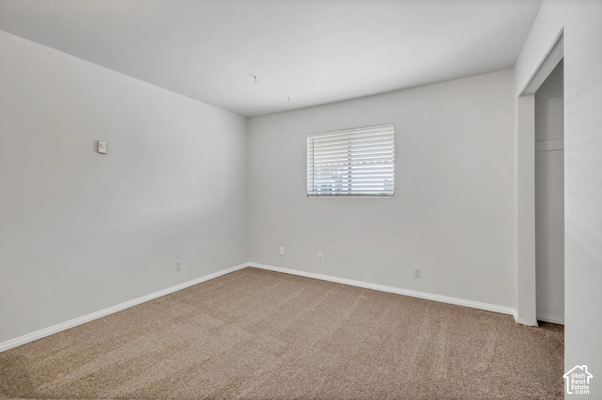 Neutral-toned interior room featuring wall-to-wall carpeting, a single window with horizontal blinds, and a built-in closet