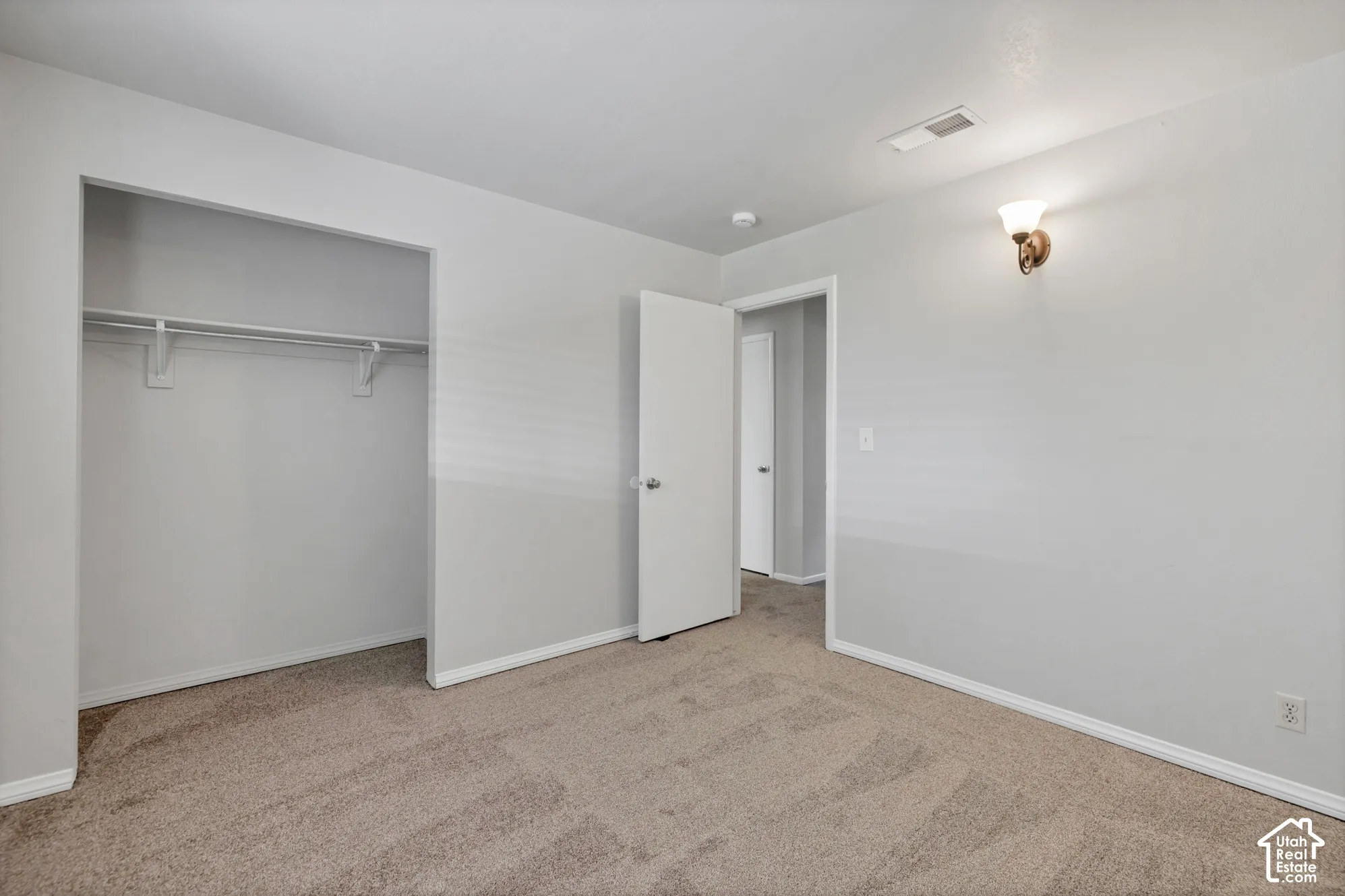 Neutral-toned interior room featuring wall-to-wall carpeting, an open-concept closet with a built-in hanging rod, and a wall-mounted light fixture