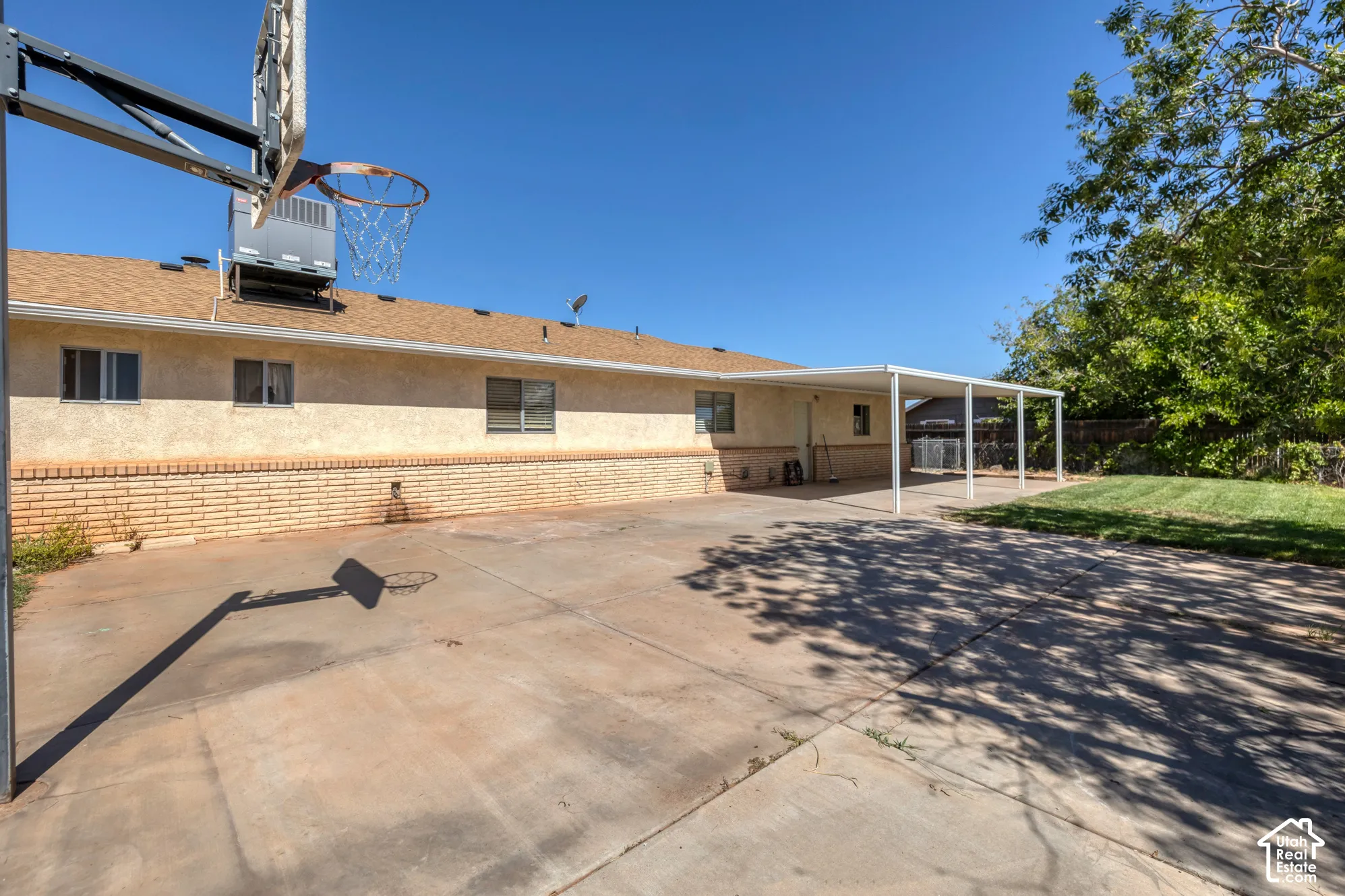 Expansive concrete patio featuring a permanent basketball hoop, a covered carport, and a brick exterior accent wall