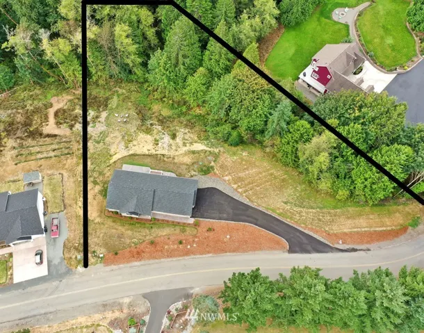 Aerial view shows the layout of the property. Paved driveway, nicely landscaped around the house, forest along the lower property line, and terraced lawn. There is a flat spot up to the right of the driveway with plenty of room to add an RV parking spot, or build that dream shop you have always wanted.