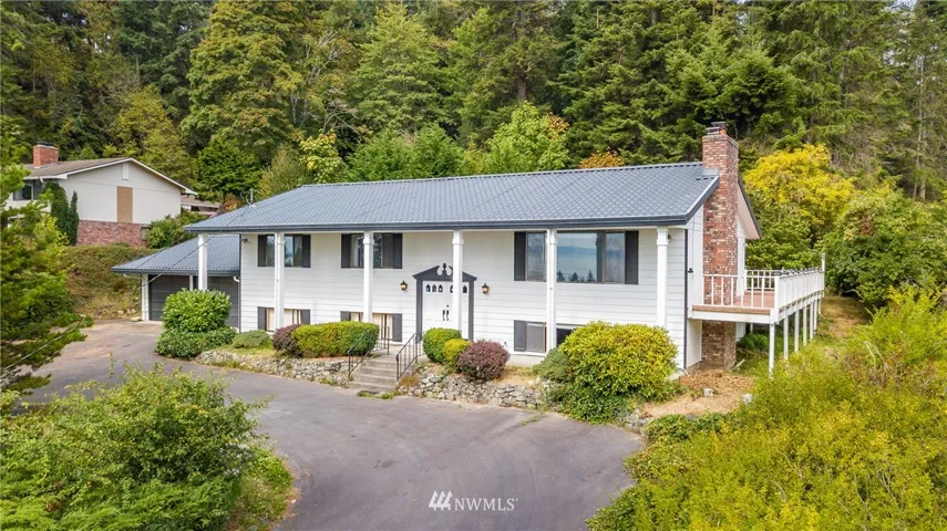 A stately home with circular driveway, metal roof and wrap around deck.