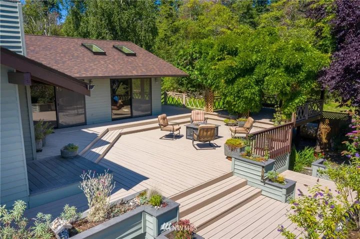 Built in raised beds frame the well maintained deck. Gardens surround below. Door on the right leads to office/second bedroom. Door to the left leads to second living room. Deck wraps around to the primary living room and master bedroom.