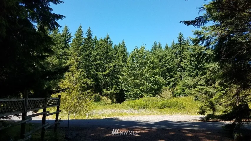 View of the lot from the neighbors drive across the street. Boundary marker is on this property; left side of drive, behind second fence post.