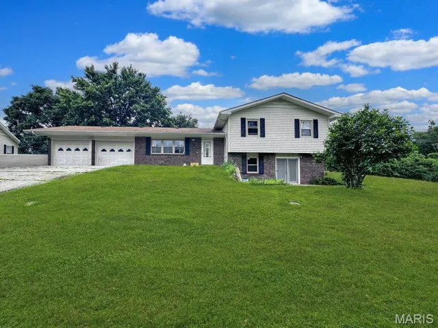 Split level home with brick siding, a front lawn, a garage, and driveway