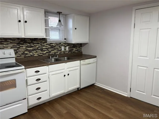 Kitchen with white appliances, white cabinetry, dark countertops, hanging light fixtures, and dark wood-type flooring