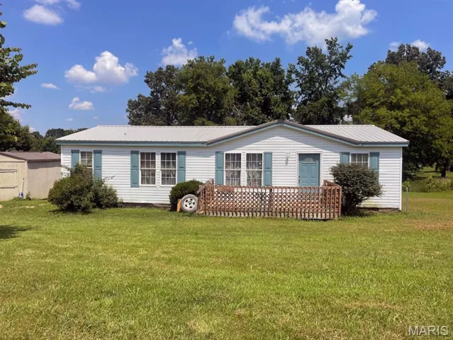 Back of property with a lawn, a metal roof, and a storage unit