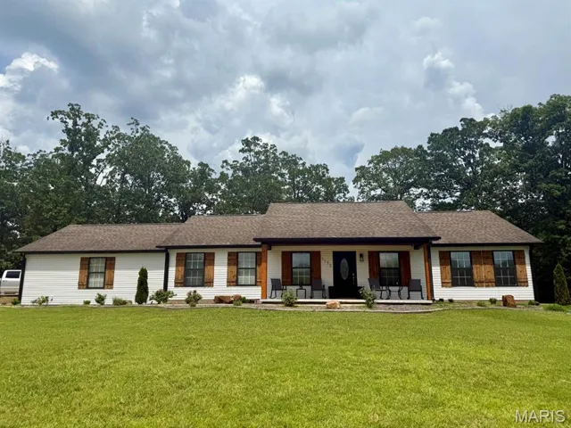 Ranch-style home featuring covered porch, a front yard, and a shingled roof