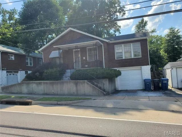 Bungalow featuring brick siding, stairway, an attached garage, covered porch, and driveway