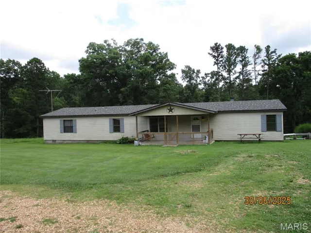Manufactured / mobile home with a porch, a front yard, and view of wooded area