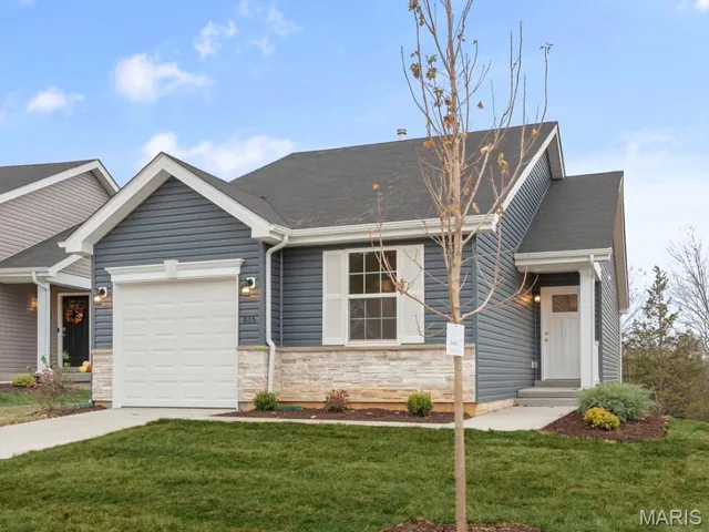 View of front facade featuring an attached garage, concrete driveway, a front lawn, and stone siding
