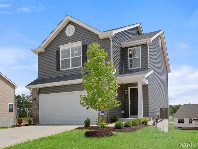 View of front of home with an attached garage, concrete driveway, and a front yard