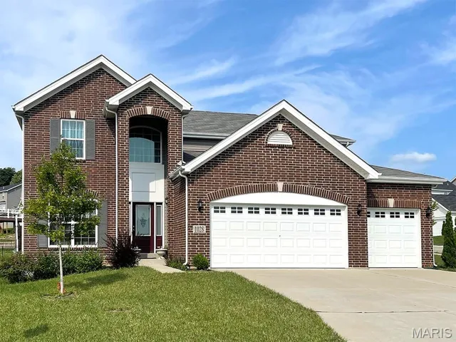 Traditional-style home with brick siding, concrete driveway, an attached garage, a front lawn, and roof with shingles