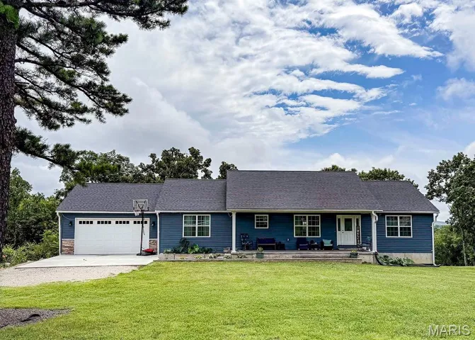 View of front of house with dirt driveway, a front lawn, a garage, and a porch