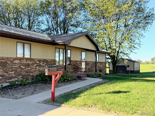 Doorway to property with brick siding, a lawn, covered porch, and a metal roof