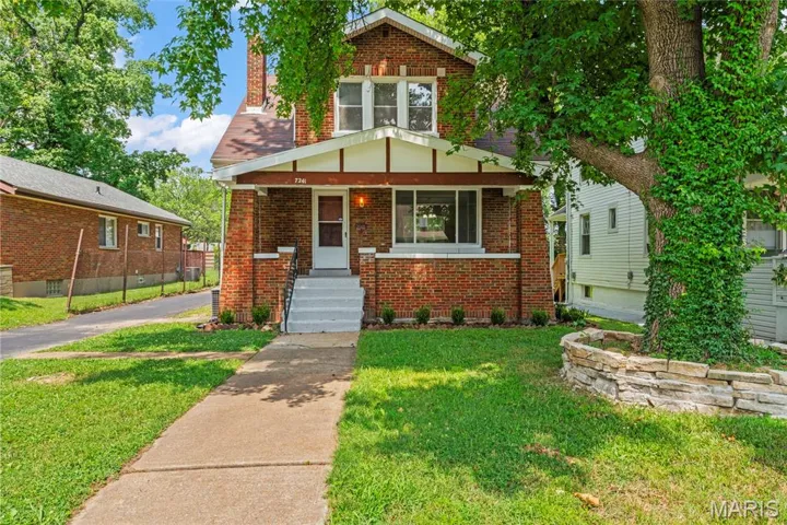 View of front of property featuring brick siding, a front yard, a porch, and a chimney