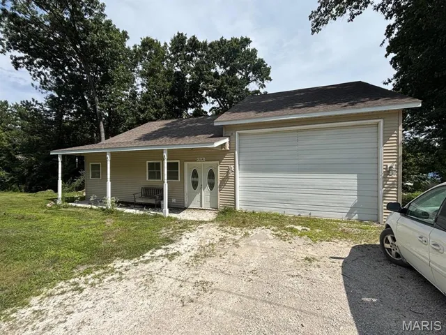 Split level home featuring roof with shingles, a garage, covered porch, and a front lawn