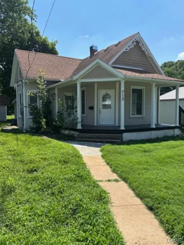 View of front of property featuring covered porch, a front lawn, roof with shingles, and a chimney