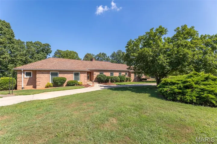 Single story home featuring a front lawn, brick siding, concrete driveway, and a chimney